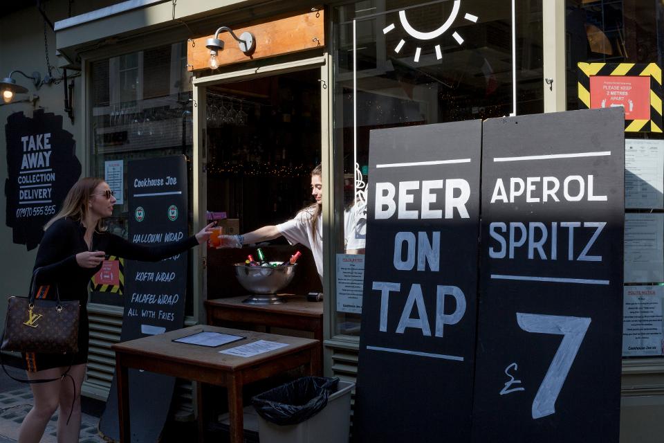 A customer orders a drink from a re-opened bar in Soho where beer on tap is available.