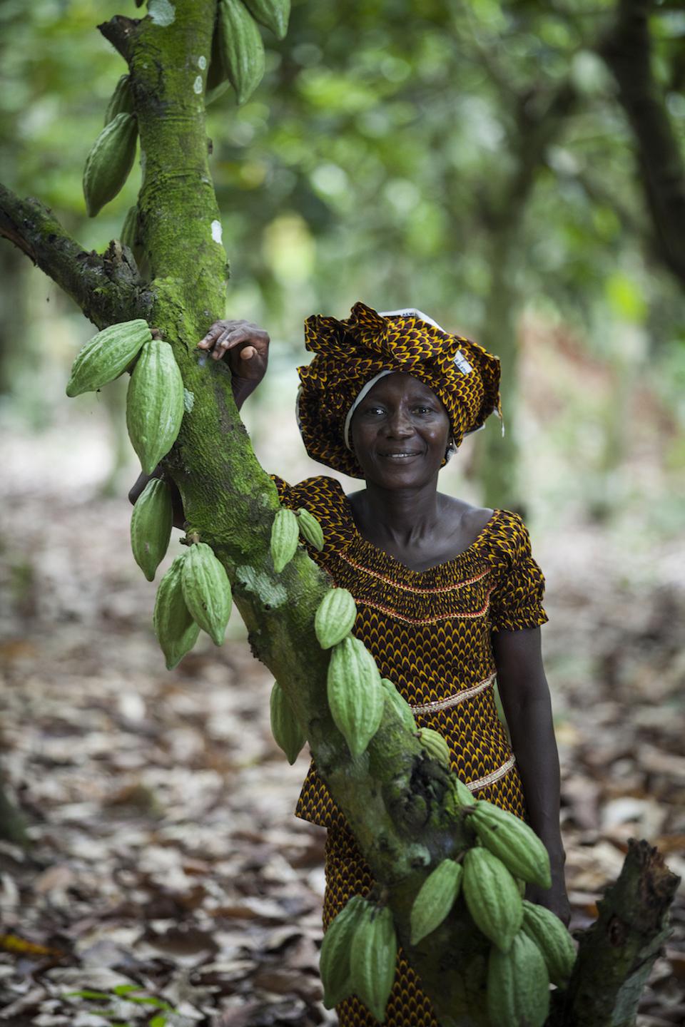 Alphonsine N'Guetia of Coopaza proudly stands next to a cocoa tree on her farm in Cote d'Ivoire. Coopaza is a Part of the Ben & Jerry's Living Income program.